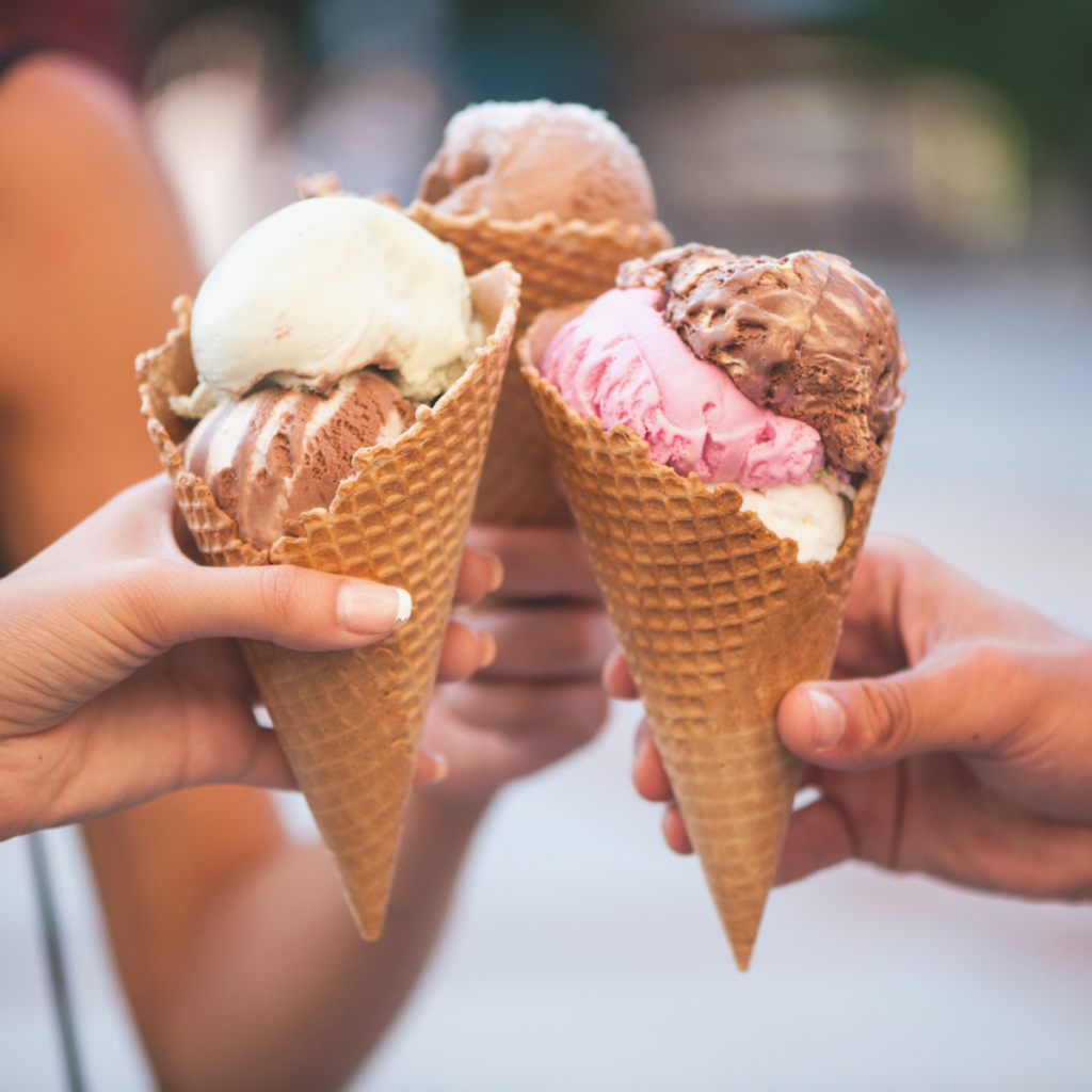 hands holding waffle cones filled with ice cream